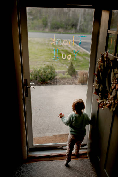 Toddler At Glass Storm Door Looking Out: Glass Has Toddler Scribbles and Thank You Message A toddler looks at the world outside her door during the coronavirus quarantine. The door has toddler marker scribbles and a thank you message written to the mail and delivery workers who come by each day. looking out front door stock pictures, royalty-free photos & images