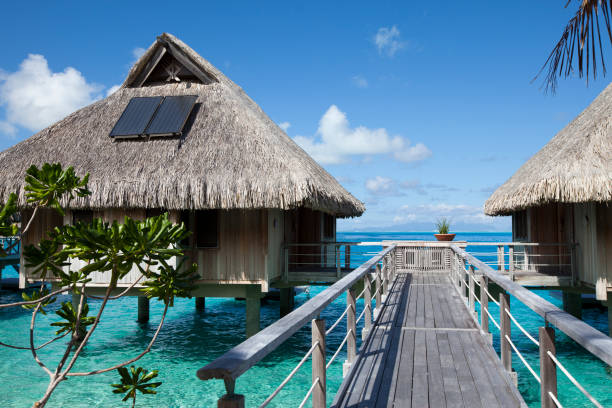 Wooden walkways over the water of the blue tropical sea to authentic traditional Polynesian thatched roof houses with eco-friendly use of solar panels. Polynesia, Tahiti stock photo