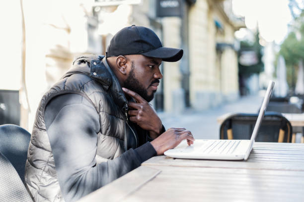 Happy black guy sitting at outdoor cafe with laptop computer