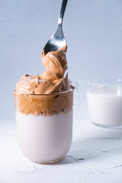 istock Dalgona coffee and whipped coffee falling from a spoon in a glass. Korean trendy, fluffy, creamed and whipped iced coffee. Vertical picture. 1218831943