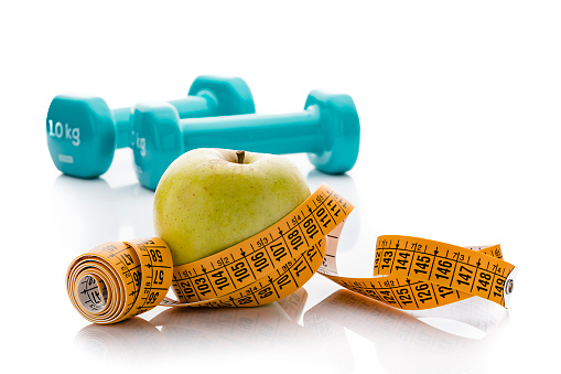 Healthy food and fitness concept: High angle view of dumbbells, apple and tape measure isolated on white background. Predominant colors are yellow and green. High resolution 42Mp studio digital capture taken with Sony A7rII and Sony FE 90mm f2.8 macro G OSS lens