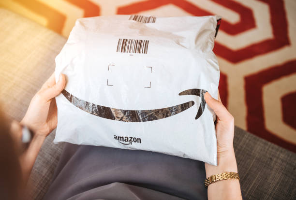 Overhead view of elegant woman on living room couch holding fresh Amazon Prime Paris, France - Aug 1, 2019: Overhead view of elegant woman on living room couch holding fresh Amazon Prime plastic package parcel with iconic logotype smile amazon.com photos stock pictures, royalty-free photos & images