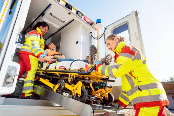 Paramedics in uniform putting injured man on stretcher in ambulance car