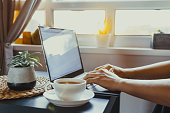 Close up man working on laptop sitting near coffee table with cup of hot drink tea. Workplace near window on sutset or early morning. Working at home. Back light, soft selective focus. Copy space.