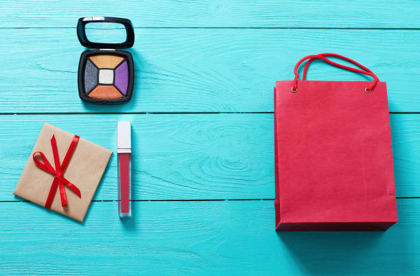 Red lipstick, eye shadows, paper bag and gift box on blue wooden background. Fashion accessories. Top view and mock up. Red lipstick, eye shadows, paper bag and gift box on blue wooden background. Fashion accessories. Top view and mock up. make over series stock pictures, royalty-free photos & images