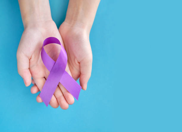 紫紫色の象徴的なリボン - 膵臓癌、嚢胞性線維症、線維筋痛の問題。青い背景に2つの交差した手 - cancer victim ストックフォトと画像