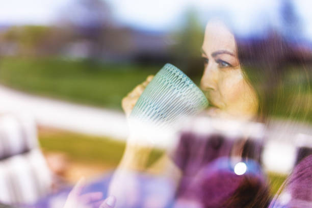 hermosa pre senior madura adulta mujer de etnia hispana en el interior a través de la ventana con taza de café - women sign love trap fotografías e imágenes de stock