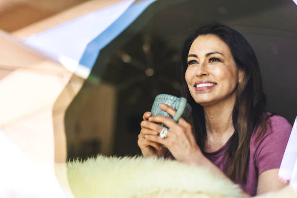 hermosa pre senior madura adulta mujer de etnia hispana en el interior a través de la ventana con taza de café - women sign love trap fotografías e imágenes de stock