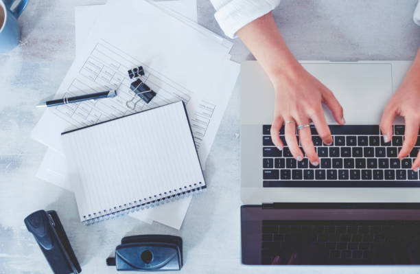 istock Top view of woman using laptop while sitting at the table with laptop, mobile phone, note pad, coffee cup. 1218851377