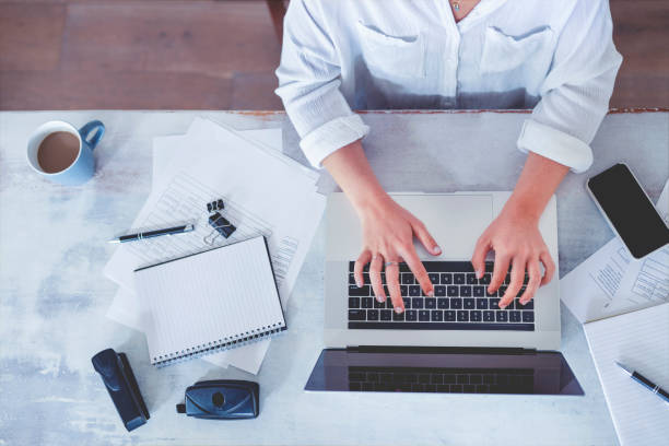 istock Top view of woman using laptop while sitting at the table with laptop, mobile phone, note pad, coffee cup. 1218851379