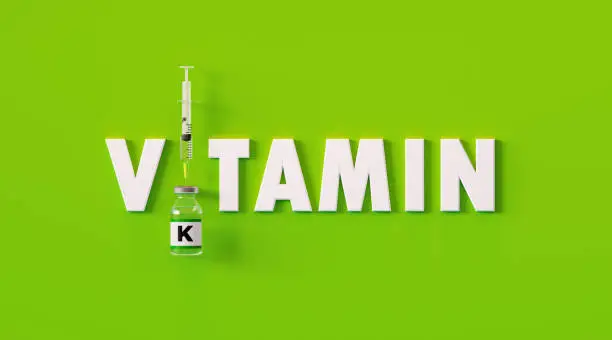 Vitamin written next to syringe and vitamin K bottle on green background, Horizontal composition with copy space. Injectable vitamin K concept.