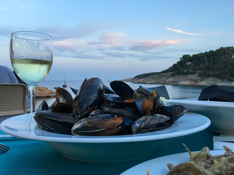 Cooked mussels with glass of white wine. Mediterranean dinner on the beach with Seaview