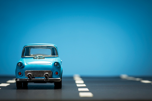 Front view of a blue toy car on on an asphalt road and a blue background.