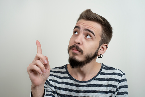 Portrait of handsome young business man having creative idea holding a finger on his lip, isolated on white background.