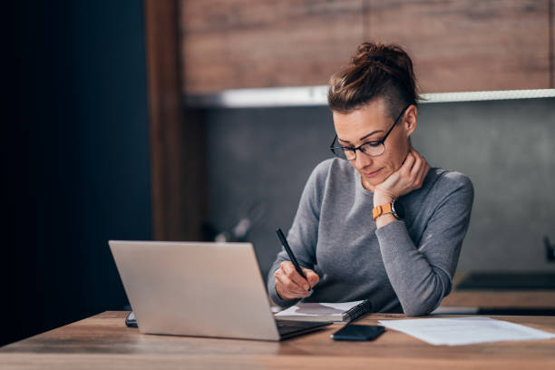 Woman at home paying the bills online from her laptop Woman at home paying the bills online from her laptop half shaved hairstyle stock pictures, royalty-free photos & images