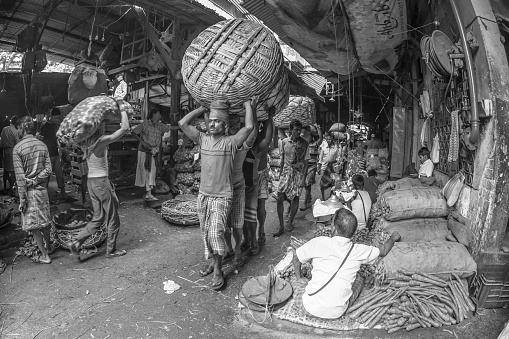 Kolkata, West Bengal, India- March 04 2017: Black and white photography of workers carrying a heavy and huge load inside Koley market,the largest wholesale vegetable market in Kolkata, India.