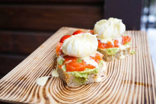 Benedict eggs with avocado and smoked salmon on a wooden board. Close-up Benedict eggs with avocado and smoked salmon, hollandaise sauce on a wooden board, close-up. hollandaise sauce stock pictures, royalty-free photos & images