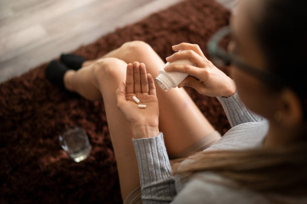 Woman Addicted to Painkillers Holding Pills in Her Hand Palm Young White Woman at home Holding Two Pain Killer Pills in Her Hand Palm After Spilling from Bottle and Glass of Water. Concept of Pain Relief, Addiction to Opioids and NSAIDs addict stock pictures, royalty-free photos & images