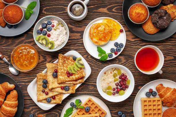 istock Continental breakfast captured from above (top view, flat lay). Coffee, tea, croissants, jam, egg, pancakes, maffins and oatmeal. Wooden background. Family breakfast table. 1218888944