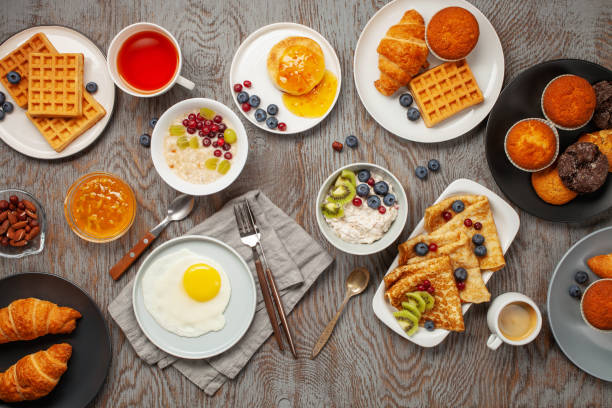 istock Continental breakfast captured from above (top view, flat lay). Coffee, tea, croissants, jam, egg, pancakes, maffins and oatmeal. Wooden background. Family breakfast table. 1218888945