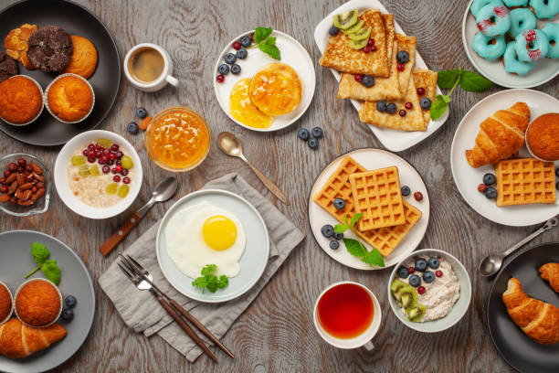 istock Continental breakfast captured from above (top view, flat lay). Coffee, tea, croissants, jam, egg, pancakes, maffins and oatmeal. Wooden background. Family breakfast table. 1218888947