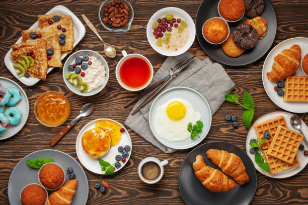 istock Continental breakfast captured from above (top view, flat lay). Coffee, tea, croissants, jam, egg, pancakes, maffins and oatmeal. Wooden background. Family breakfast table. 1218888951
