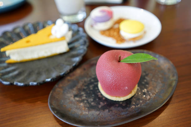Pretty red apple shape cake with green leaf on black plate on timber table