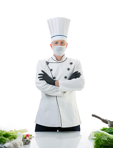 Chef cook in protective medical mask near the kitchen table. Safety and pandemic concept