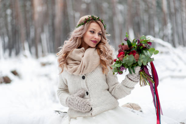 ein junges mädchen von slawischem aussehen mit einem kranz von wildblumen. schöne blonde braut hält einen blumenstrauß im winter hintergrund. - christmas wedding bride winter stock-fotos und bilder