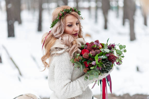 야생화화환을 들고 있는 슬라브의 어린 소녀. 아름다운 금발의 신부는 겨울 배경에 꽃다발을 보유하고 있습니다. - christmas wedding bride winter 뉴스 사진 이미지