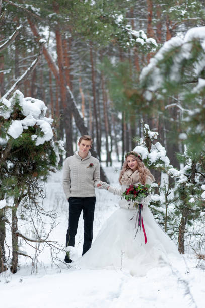 istock Cheerful bride and groom in beige knitted pullovers are walking in snowy forest. Winter wedding 1218903749