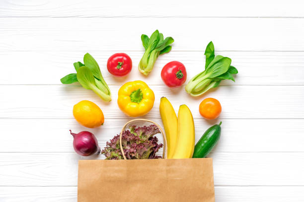 異なる健康食品の完全なエコペーパーバッグ - 黄色のピーマン、トマト、バナナ、レタス、緑、キュウリ、タマネギ白い木製の背景トップビュートップビューフラットレイ食料品の買い物 - green bell pepper green peppercorn green vegetable ストックフォトと画像