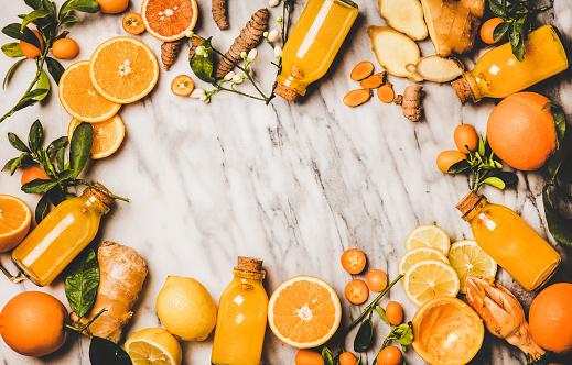 Immune boosting vitamin health defending drink. Flat-lay of fresh turmeric, ginger, citrus juice shot in glass bottles over marble background, top view, copy space. Pure vegan Immunity system booster