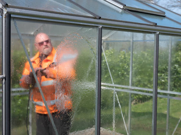 Construction worker cleaning filth with high pressure cleaner from a glass greenhouse