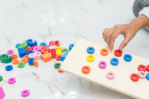 closeup of hand for girl playing color wonder blocks that a geometrical montessori puzzle of colors with constructor on floor at home, family fun at home concept