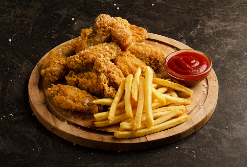 Fried chicken wings, french fries and ketchup sauce on a dark background