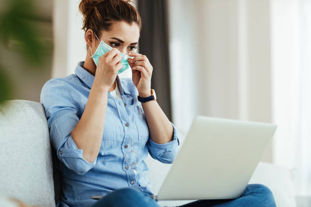 istock Woman adjusting her face mask wile using computer in the living room. 1218917715