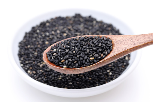 Black sesame seeds with wooden spoon. Sesame seeds in a dish on white background