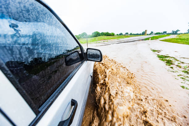 istock a white-black car rides on a road in a deep mud puddle and makes the front wheel splashes in the summer in a green field 1218920164