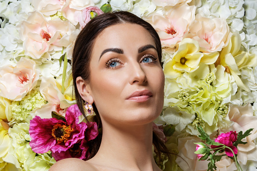 A beautiful woman's female face laying in a colourful bed of pastel white roses and other flowers