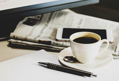 Cup of coffee with Newspaper, pen and smartphone on white table.