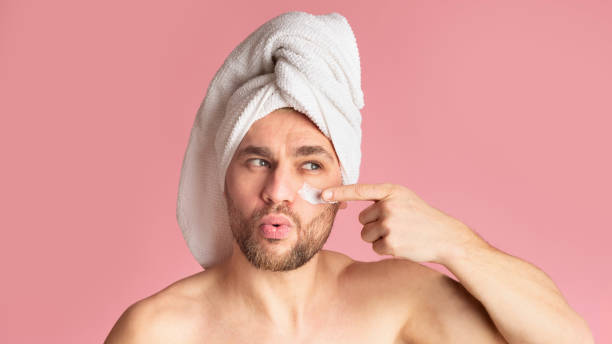 istock Guy with towel on his head smears his face with cream 1218925412