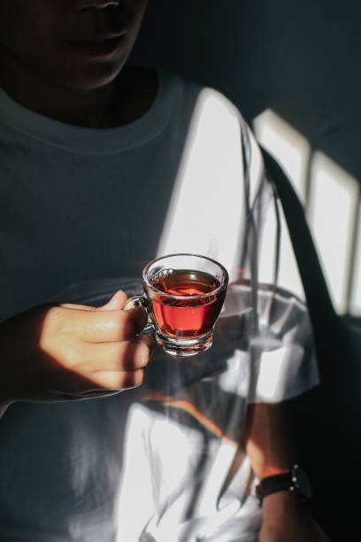 Close up man pouring hot tea from teapot  into small glass near window.Process brewing tea,tea ceremony,Cup of freshly brewed yellow or green herb tea,warm soft light, dark mood.Liquid movement in cup