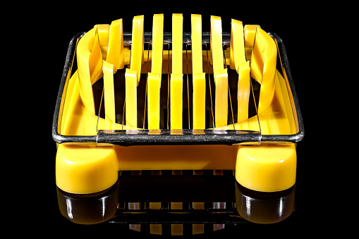 Manual yellow plastic boiled egg cutter with steel wires on the frame isolated on black background with reflection on glossy surface. Front view