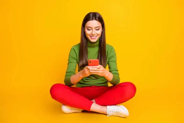 Photo of Photo of beautiful lady sit floor holding telephone hands reading popular blogger new youth theme post wear green sweater red trousers isolated yellow color background