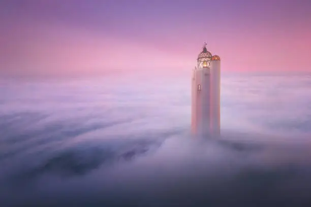 Photo of fantasy lighthouse over fog at sunset