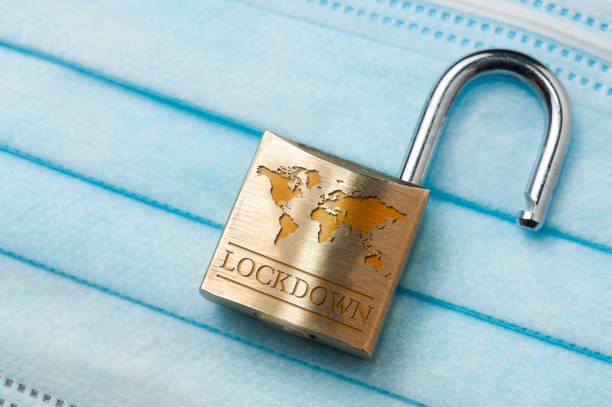 Coronavirus world lockdown end: an open lock with a world map and the word lockdown engraved on a light blue surgical mask.