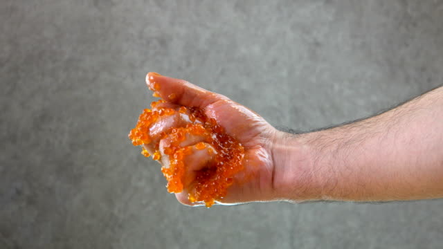 Male hand squeezes red caviar. Shows thumb up. Close-up