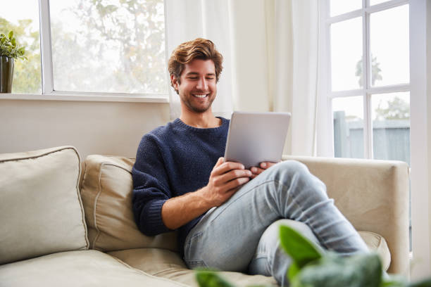 istock Smiling young man using a digital tablet on his living room sofa 1218936695