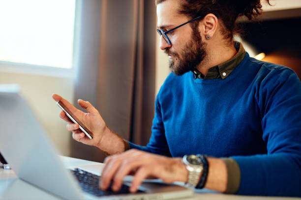 istock Attractive Caucasian bearded entrepreneur sitting in his home office, using smart phone and taking a break from work. Work from home concept. 1218936744